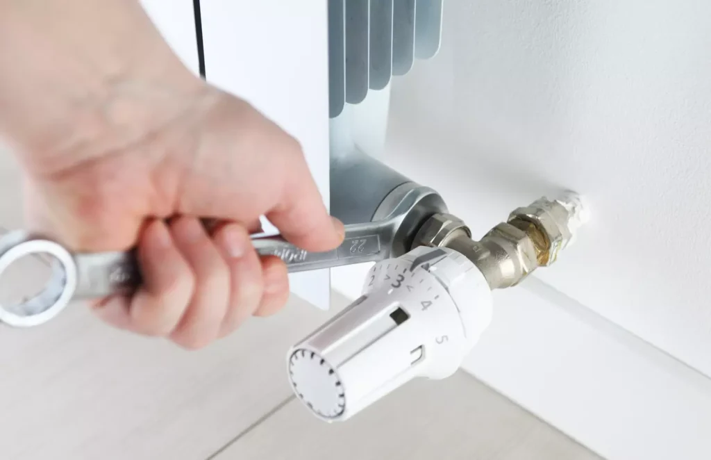 plombier serrant le robinet thermostatique d'un radiateur avec une clé plate