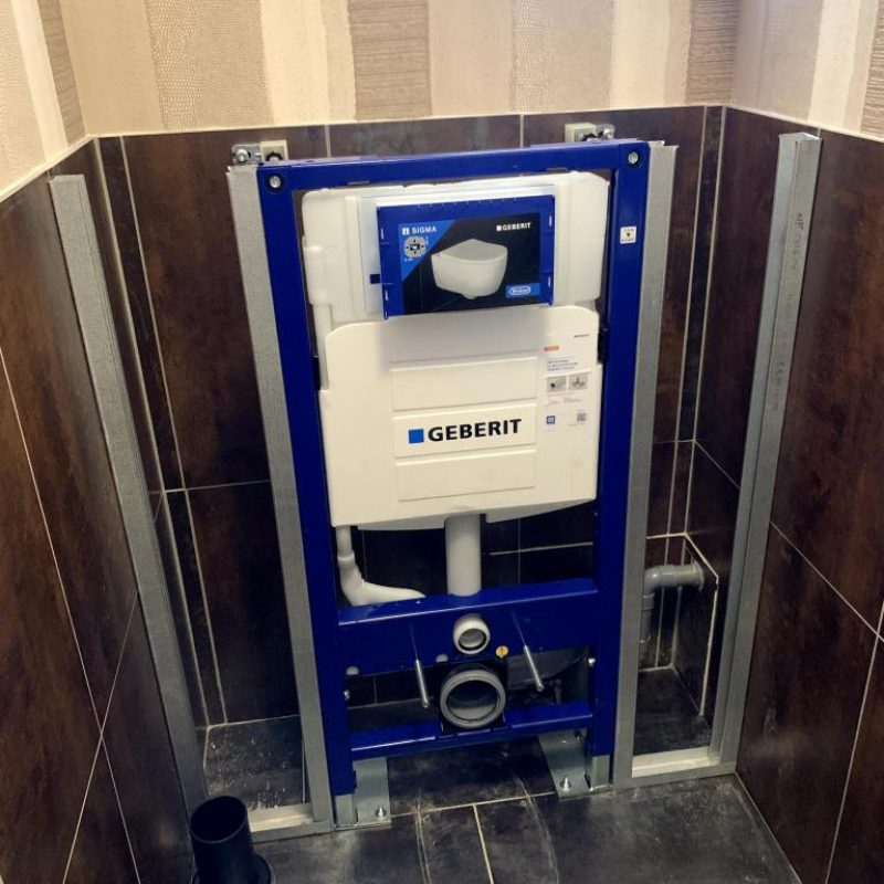 Bâti-support Geberit Sigma posé au mur dans un WC carrelé marron, prêt pour la cuvette suspendue